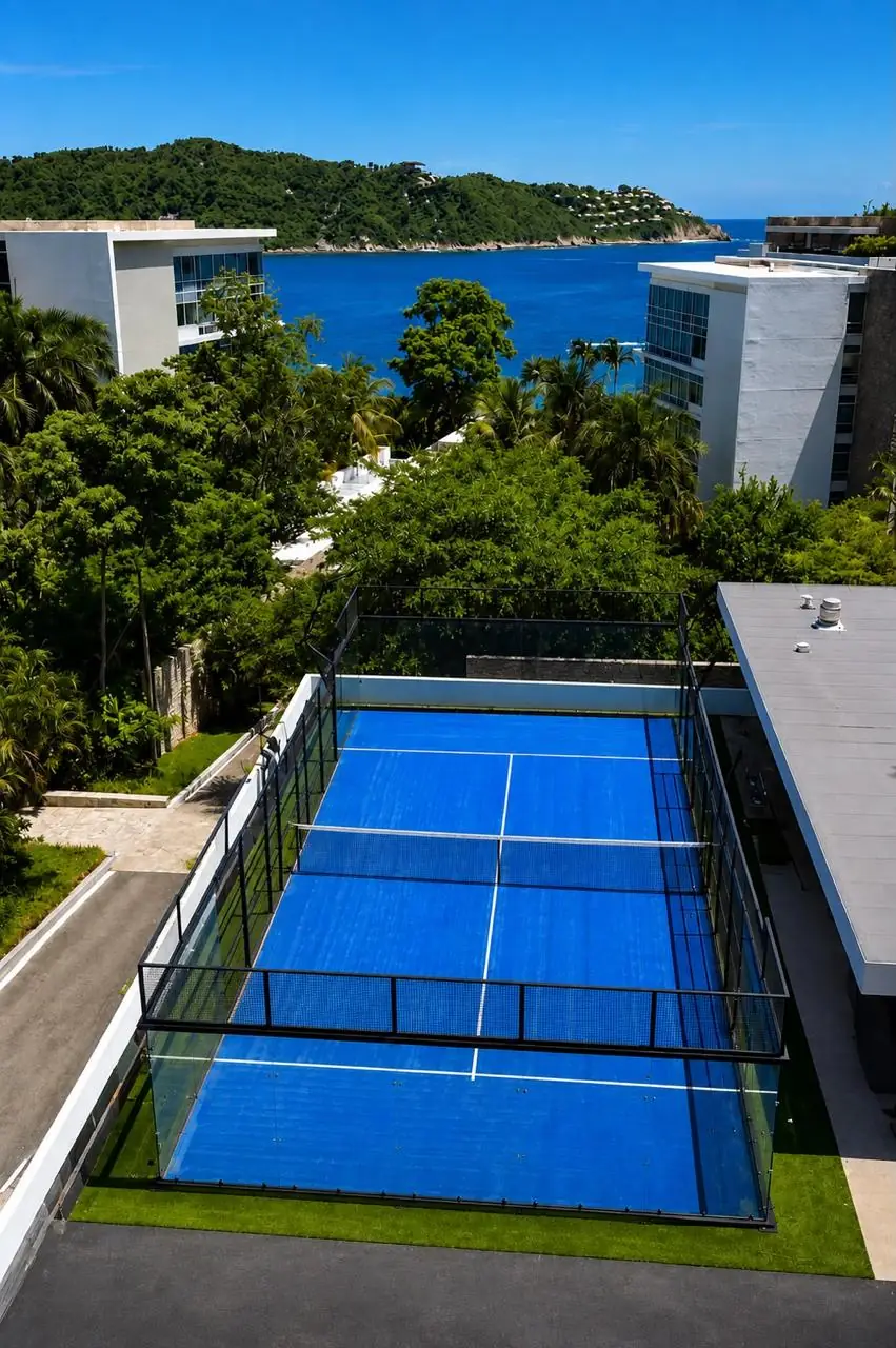 Vista aérea de una cancha de pádel panorámica azul entre edificios residenciales, con la bahía al fondo, en Guerrero