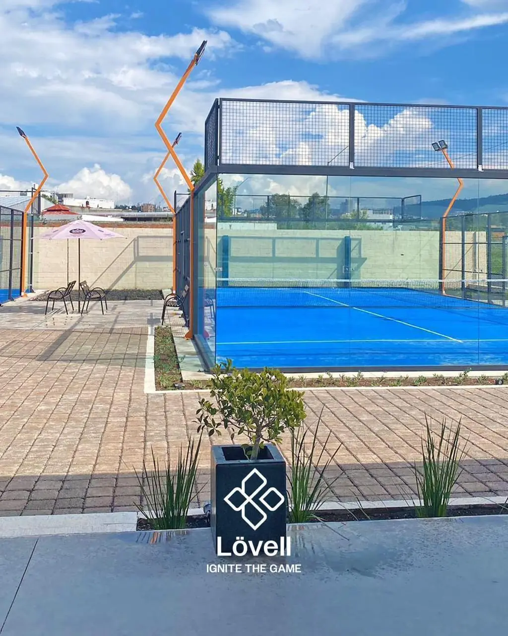 Cancha de pádel panorámica junto a una terraza con sombrilla, con postes de luz en V naranjas, en Michoacán