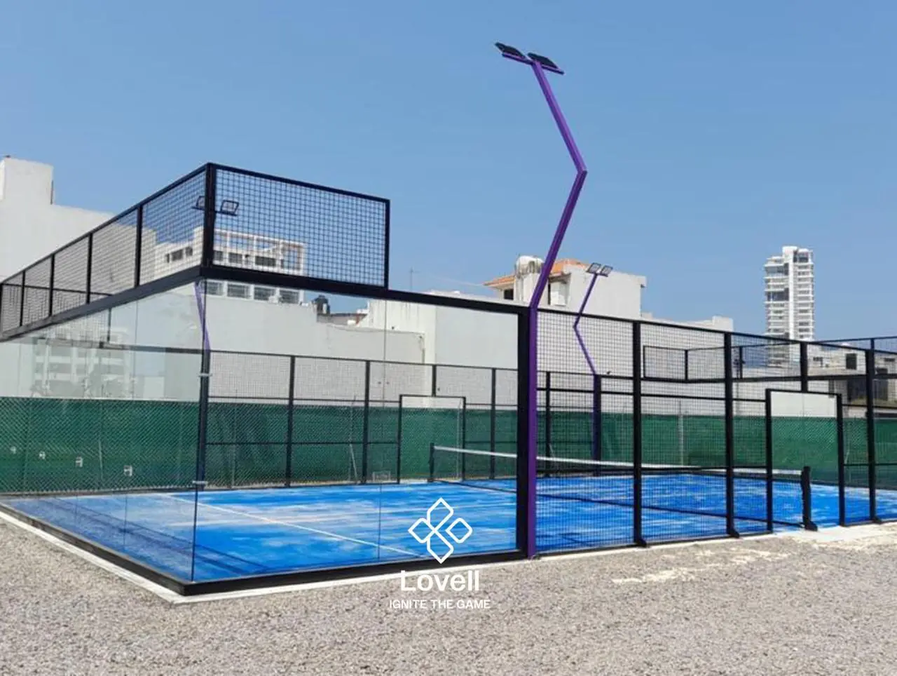 Cancha de pádel con frente de cristal y postes de luz en V morados, entre edificios, en Veracruz